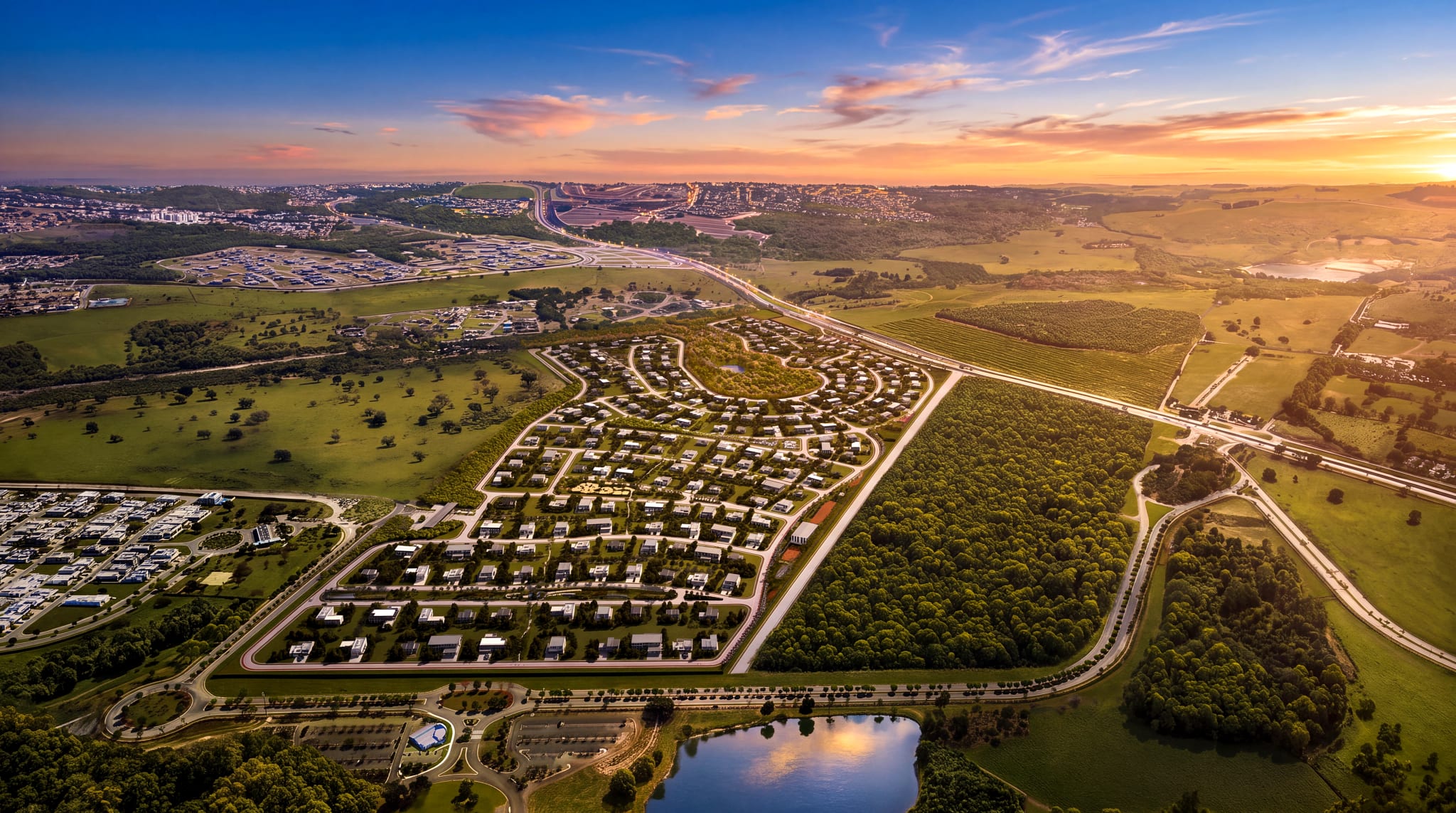 Vista aérea do loteamento ao entardecer, com o eixo rodoviário ao fundo